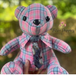 May include: A handmade teddy bear with a pink, blue, and white plaid pattern. The bear has black button eyes and a black nose. It is wearing a collared shirt and a patterned tie. The text "Three Poppies Creations" is visible.