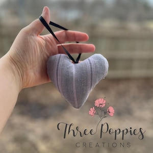 May include: A gray and white striped heart-shaped fabric sachet with a black ribbon. The sachet is held in a hand. The image includes the text "Three Poppies Creations".
