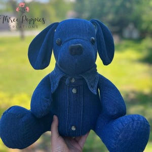 May include: A handmade blue denim dog plush toy with button details. The dog has large floppy ears and a button-down denim jacket. The text "Three Poppies Creations" is visible in the upper left corner.
