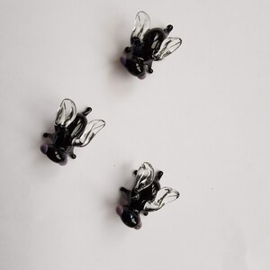 May include: Three black glass fly figurines with clear wings. The flies are posed with their wings spread out.