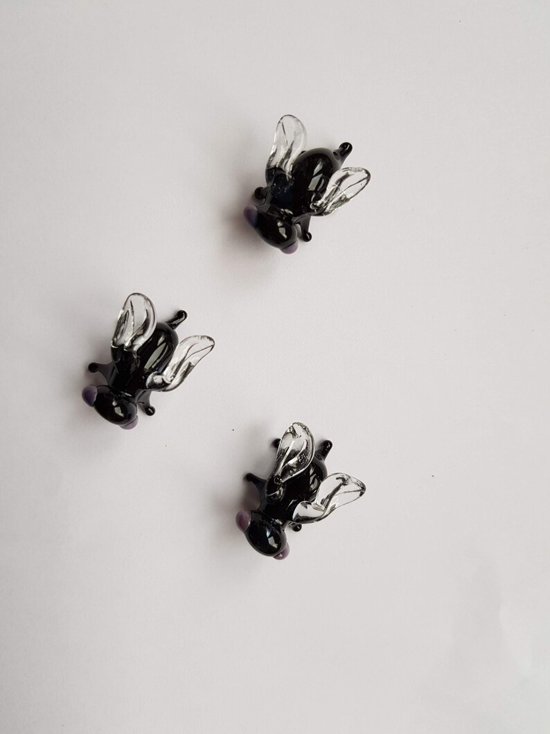 May include: Three black glass fly figurines with clear wings. The flies are posed with their wings spread out.