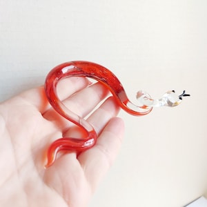 Op de afbeelding: Een rood glazen slangbeeldje met een helder glazen kop en zwarte ogen. De slang is opgerold in een spiraalvorm.