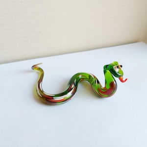 Op de afbeelding: Een groene glazen slangfiguur met rode en witte accenten. De slang is in een S-vorm gekruld met zijn kop omhoog en tong uitgestoken.