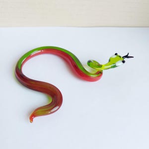 May include: A green and red glass snake figurine with white eyes. The snake is curled in an S shape.