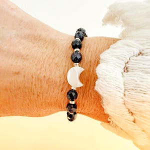 May include: A beaded bracelet featuring dark blue, faceted, glittery sandstone beads alternating with small silver-toned spacers and a central white, crescent moon-shaped charm made of a smooth, opaque material.