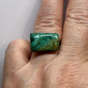 May include: A rectangular ring with a vibrant green and brown stone. The stone has a marbled appearance with varying shades of green and brown. The ring is a statement piece, showcasing the natural beauty of the stone.