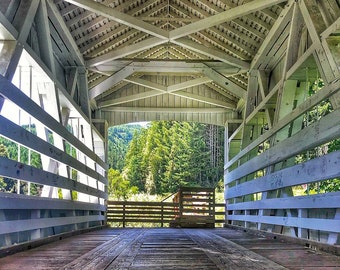 Könnte beinhalten: Eine weiße, überdachte Holzbrücke mit einem Holzboden und Blick auf einen Wald durch die Öffnung.
