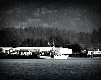 May include: A black and white photo of a fishing boat docked at a pier. The boat is in the foreground and the pier is in the background. The boat is a small, wooden vessel with a cabin and a mast. The pier is made of wood and has a railing. The photo was taken on a cloudy day.