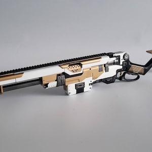 Puede incluir: Un rifle de estilo futurista con una combinación de colores blanco, dorado y negro. El rifle presenta un cañón largo con acabado negro, un cuerpo blanco con detalles dorados y una culata negra. El diseño incorpora formas geométricas y una estética moderna.