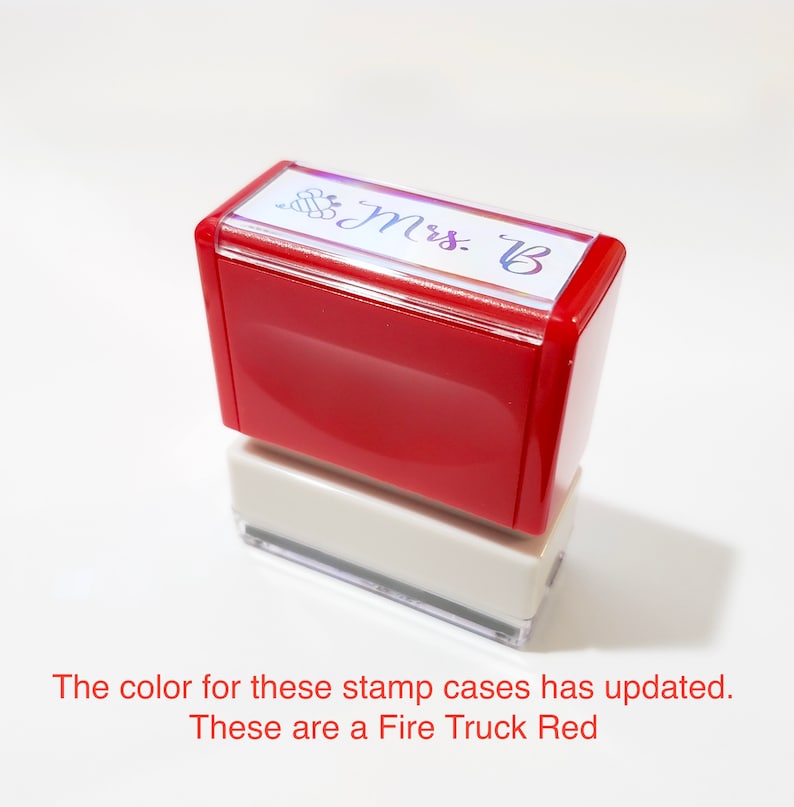 May include: A rectangular self-inking stamp with a bright fire truck red casing and a white base. The top of the stamp features a clear label with a small bee icon and the text Mrs. B printed in a dark script font on a white background.