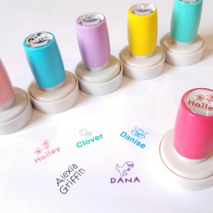May include: Six colorful self-inking stamps with different designs and names, including "Alexia Griffin", "Hailey", "Clover", "Danise", and "Dana".