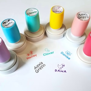 May include: Six colorful self-inking stamps with white bases and cylindrical handles in purple, blue, teal, yellow, light pink, and dark pink. Each handle features a name and icon: Danise, Ruffin, Clover, DANA, Alexia Griffin, and Hailey.