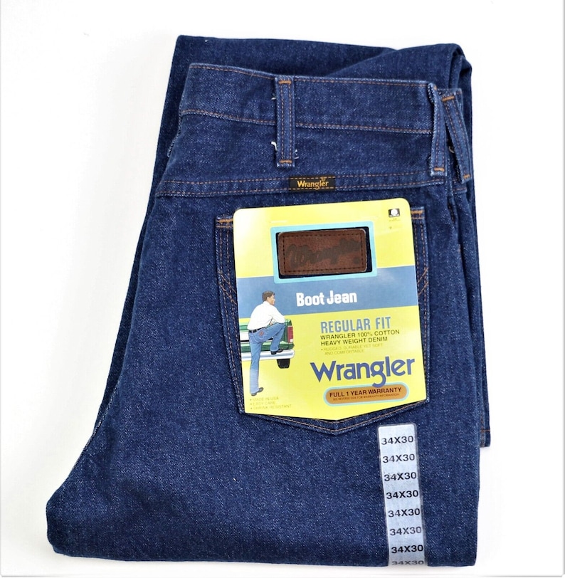 May include: A pair of blue denim jeans with a yellow and brown Wrangler label attached. The label says "Boot Jean" and "Regular Fit" and includes the text "Wrangler 100% Cotton Heavy Weight Denim".