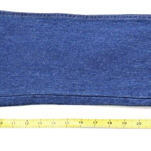 May include: A close-up of a pair of blue denim jeans with a yellow measuring tape placed along the bottom edge. The tape measures 30 inches in length.