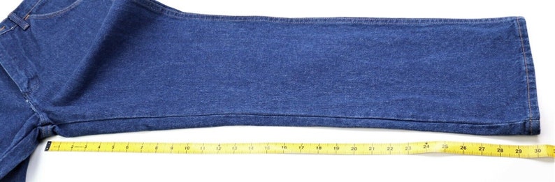 May include: A close-up of a pair of blue denim jeans with a yellow measuring tape placed along the bottom edge. The tape measures 30 inches in length.