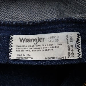 May include: A white Wrangler jeans care label with black text. The label includes the size 34 x 30, the style number 945WHD, and the care instructions: Machine wash with like colors, only non-chlorine bleach when needed, tumble dry, remove promptly. The label also states Made in USA and 100% Cotton.