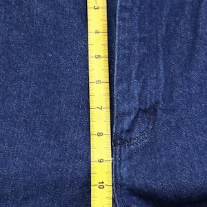 May include: A close-up of a pair of blue denim jeans with a yellow measuring tape running vertically along the side seam. The tape measures up to 14 inches.