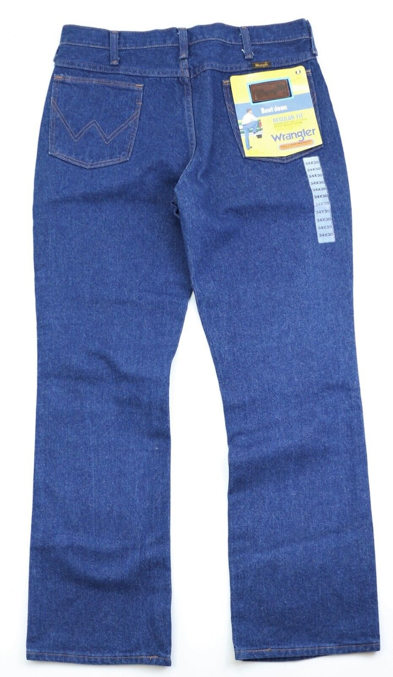 May include: A pair of blue denim jeans with a bootcut leg opening. The jeans have a back pocket with a stitched 'W' logo. The jeans have a tag attached that says 'Bootcut Regular Fit Wrangler'.