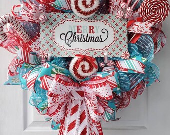 May include: A decorative Christmas wreath featuring red and turquoise mesh, white and red striped ribbons, and peppermint candy accents. A central rectangular sign displays the text Merry Christmas in black and red script, surrounded by a pattern of small red and turquoise candies.