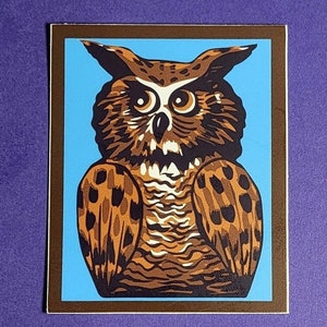 Peut inclure: Illustration stylisée d'un hibou aux plumes marron et beige, sur fond bleu clair. Le hibou est encadré d'une bordure marron, créant un contraste saisissant. L'œuvre présente des motifs détaillés et un regard concentré.