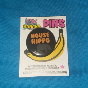 May include: A black and yellow pin with a black circle featuring the text "HOUSE HIPPO" in orange letters. A black silhouette of a hippopotamus is shown walking on a path of brown dots. The pin is on a white background with the text "Rad Banana Pins" and "All Rad Banana Merch is Designed and Made in Canada. E78V.COM/RADBANANACANADA" in black text.
