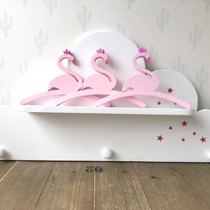 Pode incluir: Prateleira de madeira branca em forma de nuvem com decorações de flamingos cor-de-rosa e estrelas cor-de-rosa. A prateleira tem dois ganchos na parte inferior e uma pequena prateleira na parte superior.