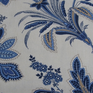 May include: Close-up of a fabric with a repeating floral pattern. The design features large, stylized flowers and foliage in shades of blue and tan against a light beige background. The fabric has a textured appearance.