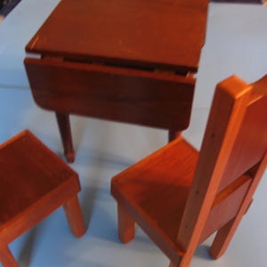 May include: A set of wooden furniture, including a drop-leaf table and two chairs. The table and chairs are all made of a dark wood and have a simple, rustic design.