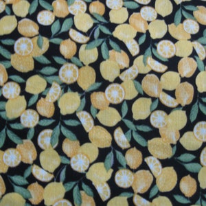 May include: A black fabric with a repeating pattern of yellow lemon slices. The lemons are arranged in a random pattern and are cut into various shapes.