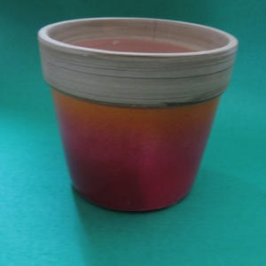 May include: A terracotta candle holder with a white and orange ombre glaze. The holder has a round shape and a smooth, slightly textured surface.