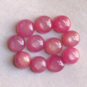 May include: A collection of eleven small, round, cabochon-cut gemstones in a vibrant shade of pink. Each stone features a smooth, polished, domed surface that reflects light, creating a glossy appearance across the uniform circular shapes.