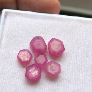 Può includere: Sei gemme esagonali rosa con un interno più chiaro sono esposte su una superficie bianca. Le gemme hanno una qualità traslucida e il colore rosa varia in intensità. Le gemme sono di dimensioni variabili.
