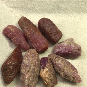 Peut inclure: Une collection de pierres précieuses rubis brutes et non taillées. Les pierres varient en taille et en forme, affichant des nuances de rouge, de brun et de rose. Les pierres précieuses ont un aspect naturel et non poli, avec des textures et des imperfections visibles.