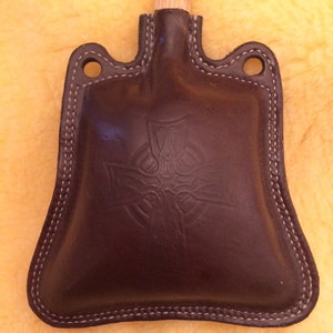 May include: A brown leather flask with a Celtic knot design and a wooden stopper.