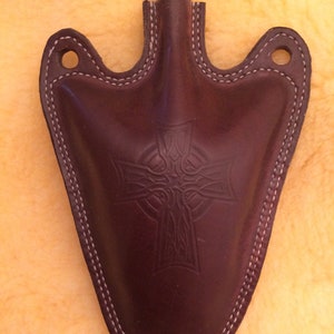 May include: A brown leather flask with a Celtic cross design and a wooden stopper. The flask has a pointed bottom and a stitched edge.