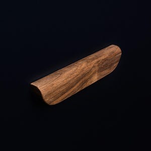 May include: A wooden drawer pull with a curved shape and a dark brown wood grain.