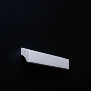 Może przedstawiać: Biały uchwyt do drzwi szafki o lekko zakrzywionym kształcie.