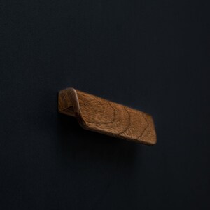 Puede incluir: Un tirador de cajón de madera marrón oscuro con un diseño curvo.