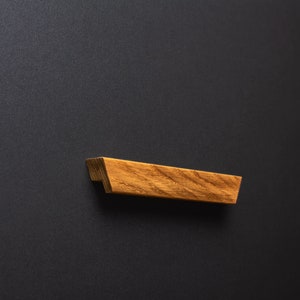 May include: A wooden drawer pull with a natural wood finish and a rectangular shape.