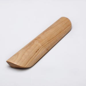 May include: A light-colored wooden rolling pin with a rounded top and a flat, angled bottom. The rolling pin is made of a light-colored wood and is set against a white background.