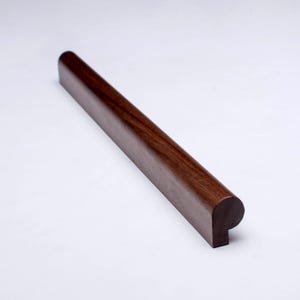 May include: A rectangular, dark brown wooden handrail section with a rounded top and a squared-off end. The wood grain is visible, and the surface has a smooth, polished finish. The handrail is designed for a staircase or similar structure.