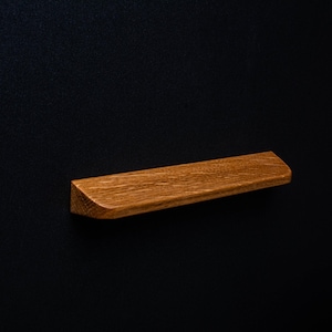 May include: A wooden cabinet pull with a curved edge and a natural wood finish.