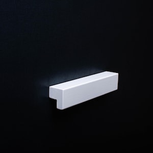 May include: White rectangular cabinet pull with a T-shaped design.