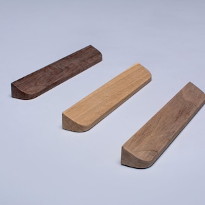 Może przedstawiać: Trzy drewniane uchwyty o zaokrąglonych krawędziach. Uchwyty są wykonane z różnych rodzajów drewna, w tym orzecha włoskiego i dębu.