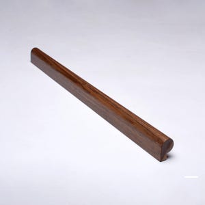 Può includere: Un corrimano in legno marrone scuro, di forma rettangolare con estremità arrotondate. La venatura del legno è visibile. Il corrimano è leggermente inclinato. Progettato per uso domestico o commerciale.