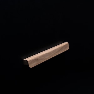 Może przedstawiać: Drewniany uchwyt do szuflady o zakrzywionym kształcie. Uchwyt jest jasnobrązowy i ma gładkie wykończenie.