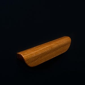 Pode incluir: Uma puxador de gaveta de madeira com forma curva e acabamento em madeira natural.