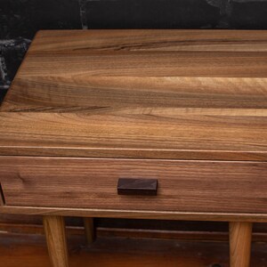 May include: A wooden nightstand with a single drawer and a dark brown wooden knob. The nightstand has a light brown wood finish and sits on four legs.