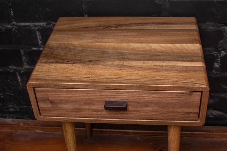 May include: A wooden nightstand with a single drawer and a dark brown wooden knob. The nightstand has a light brown wood finish and sits on four legs.