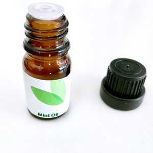 May include: A small amber glass bottle of mint oil with a white label and green leaf design. The bottle has a white cap and a separate black cap. The words "Mint Oil" are printed on the label.